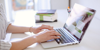 Arbeit am Laptop Studentin tippend am Laptop, daneben liegen Bücher und Stifte.